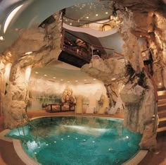 an indoor swimming pool in the middle of a room with rocks on the wall and stairs leading up to it