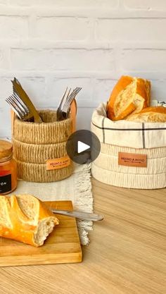 bread and butter are sitting in baskets on a wooden table with utensils, knifes and spoons