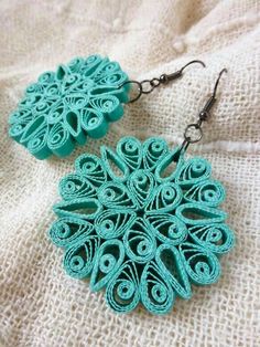 a pair of earrings made out of paper on top of a white cloth covered surface