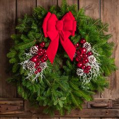 a christmas wreath on a wooden wall with red and white berries, pine cones, evergreen leaves and snowflakes