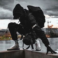 a man in black hoodie and white sneakers on top of a wall with his back to the camera