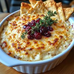 a white bowl filled with cheese and cranberries next to crackers on a wooden table