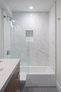 a bathroom with marbled walls and flooring is pictured in this image, there is a bathtub next to the shower