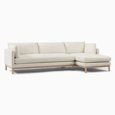 a white sectional couch with wooden legs and pillows on it's back end, in front of a white background