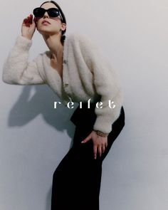 a woman in black pants and white sweater leaning against a wall with her hand on her head