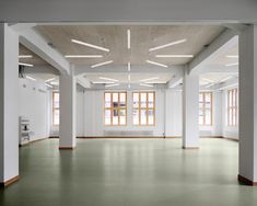 an empty room with white columns and green flooring, in front of two windows