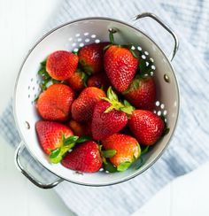 a bunch of strawberries in a colander on a white tablecloth with a blue towel