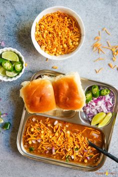 two trays filled with food next to bowls of vegetables and bread on a table