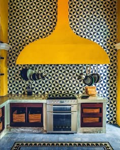 a kitchen with yellow walls and black and white tiles on the wall, an oven in the center