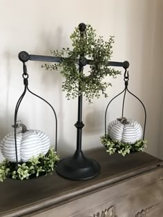 two white pumpkins sitting on top of an iron stand with greenery in them