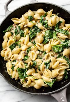 a skillet filled with pasta and spinach on top of a marble countertop