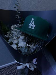 a baseball cap sits on top of a bouquet of flowers in a triangular shaped box