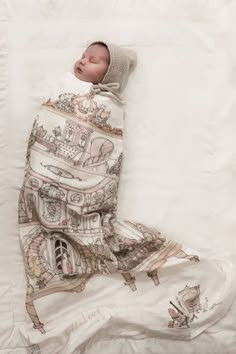 a baby wrapped in a blanket sleeping on top of a white sheet with an image of a building