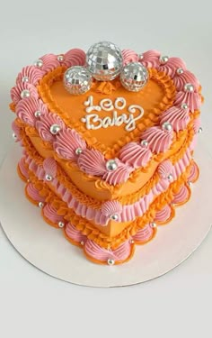 a heart shaped cake is decorated with pink and orange icing, two silver balls on top