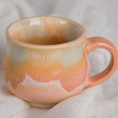 an orange and white cup sitting on top of a white cloth covered tablecloth,