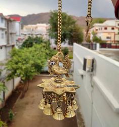 a gold bell hanging from a chain in front of a building with trees and buildings behind it