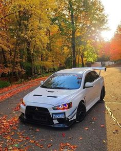 a white car parked on the side of a road in front of trees with fall leaves