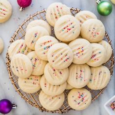 a basket full of cookies with sprinkles next to christmas ornaments and baubles