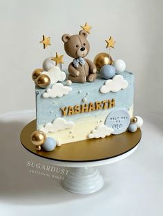 a teddy bear sitting on top of a blue and white cake with gold stars around it