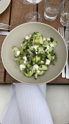 a white bowl filled with cucumbers on top of a table next to silverware