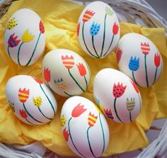 six painted eggs in a wicker basket on a table top with yellow tissue paper