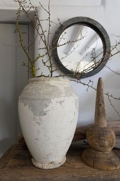 a white vase sitting on top of a wooden table next to a mirror and plant