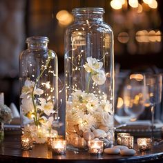 flowers and candles are in glass vases on a round table with lights around them