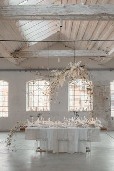 the table is set with white linens and flowers in front of two large windows