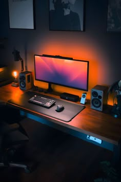 A moody and inviting home office featuring a desk with vibrant orange backlighting illuminating against a dark room. Artistic prints adorn the walls, complementing the sleek, modern aesthetics of the setup that includes a widescreen monitor, a mechanical keyboard, and various desktop speakers, all under soft, ambient lighting. Standing Desk With Storage, Standing Desk Setup, Moody Home Office, Gaming Computer Room, Standing Desk Adjustable, Desk Adjustable Height, Warm Ambient Lighting, Setup Pc, Moody Home