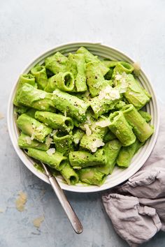 a white bowl filled with green pasta on top of a blue table cloth next to a spoon