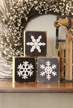 three wooden blocks with snowflakes on them are sitting on a mantle in front of a wreath