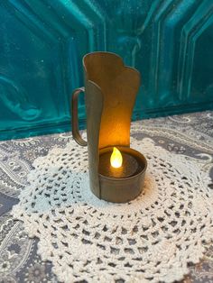 a candle is lit in a tea light holder on a doily with a blue background