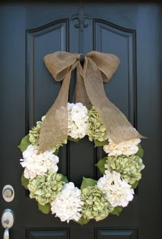 a wreath with flowers and burlocks is hanging on the front door's black door