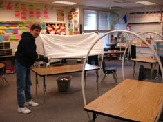 a man standing next to a table with a white sheet on it in a classroom