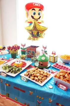 a table topped with lots of food next to a giant paper mario mushroom balloon hanging from the ceiling