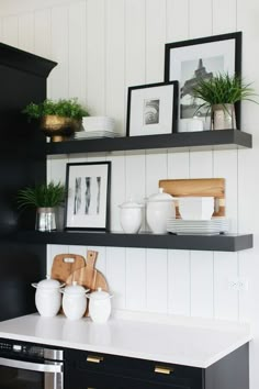 black and white kitchen shelves with pictures on them, plants and utensils in vases