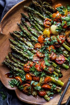 asparagus, tomatoes and other vegetables on a wooden platter with a fork