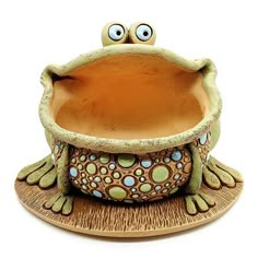 a ceramic frog sitting on top of a saucer with eyes wide open and mouth wide