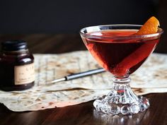 a glass filled with red liquid sitting on top of a table next to a bottle