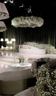 a living room filled with lots of furniture and flowers hanging from the ceiling next to lamps