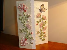 two cards with flowers and butterflies on them sitting on a table next to a lamp