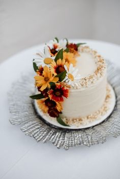 a white cake with flowers on top is sitting on a silver platter and sits on a table