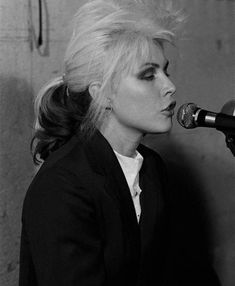 a black and white photo of a woman with blonde hair singing into a microphone in front of a wall