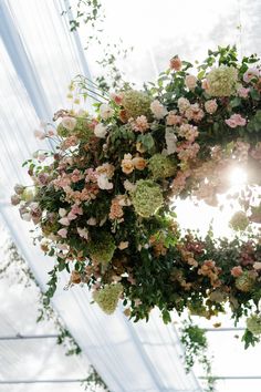 a floral wreath hanging from the ceiling in front of a white wall with green and pink flowers