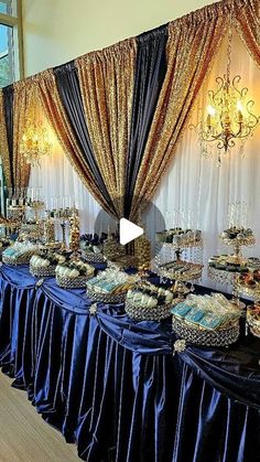 a table with many desserts on it in front of a curtain and chandelier