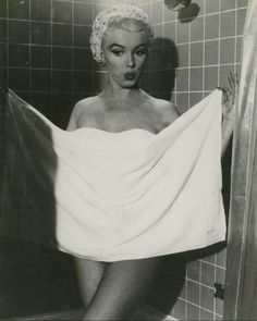 a woman in a bathrobe is standing next to a shower with her hand on the curtain