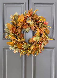 a wreath on the front door with autumn leaves and berries hanging from it's side