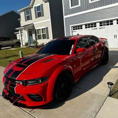 a red sports car parked in front of a house with black stripes on the hood