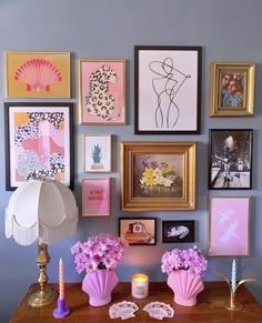 a wooden desk topped with lots of pictures and pink flowers in a vase next to a lamp