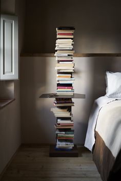 a tall stack of books sitting next to a bed